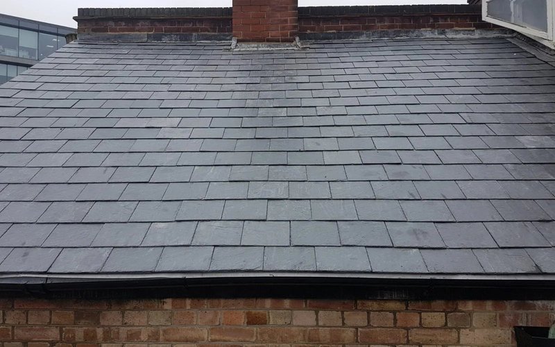 Completed grey slate roof beside a brick chimney