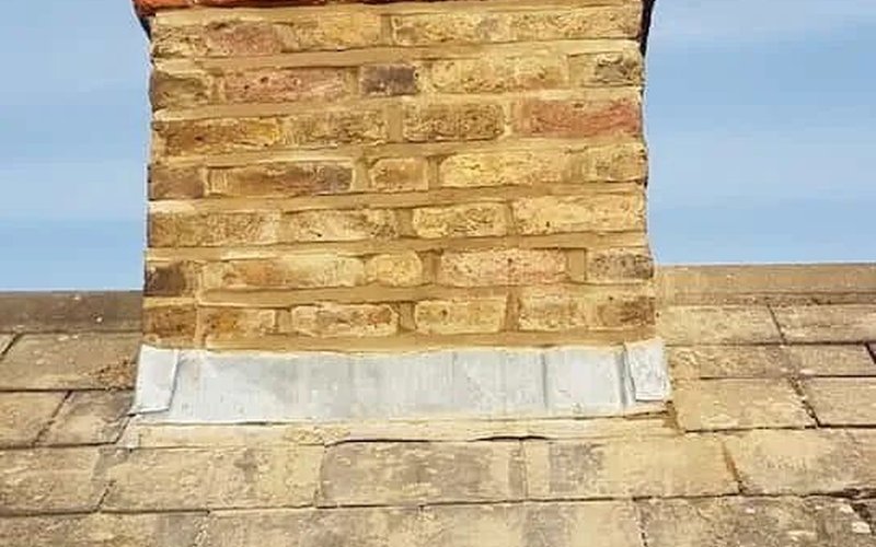 Weathered brick chimney stack and lead flashing at the roof junction