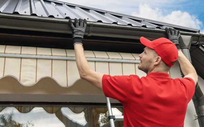 Roofer working on a rainwater gutter beside a tiled roof