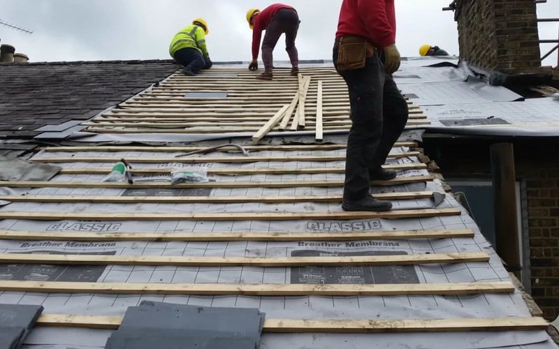 Roofer laying slate tiles onto battens during roof installation