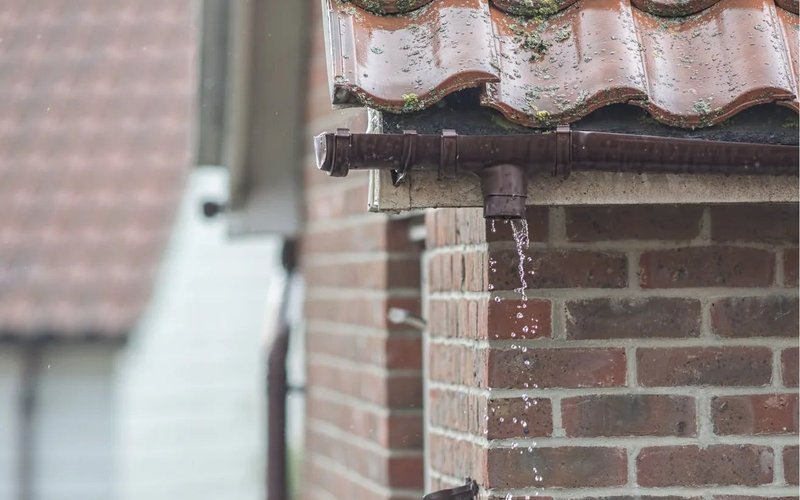 Gutter joint at the edge of a tiled roof beside brickwork