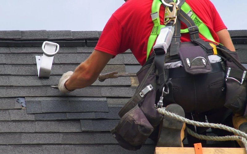 Roofer examining grey slate roof coverings beside a roof vent