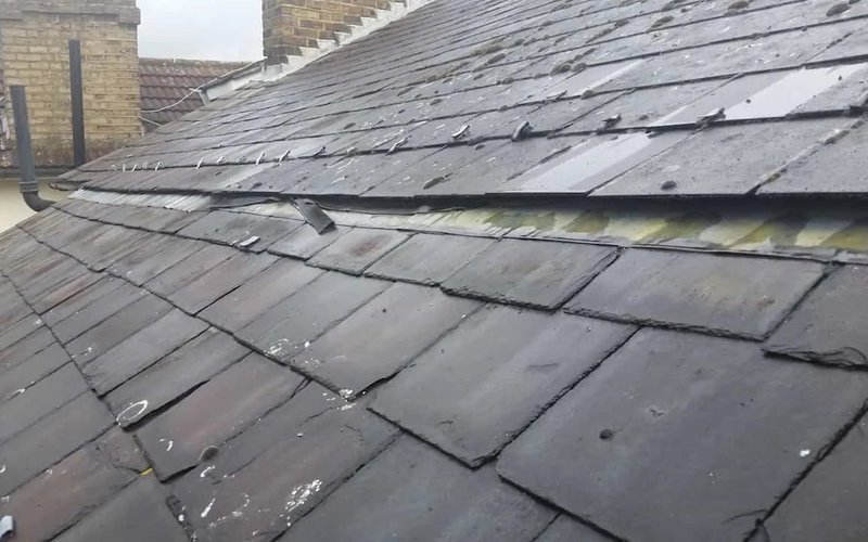 Loose and broken grey slate tiles on a pitched roof