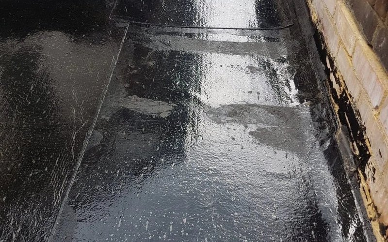 Dark flat roof waterproofing beside an external wall abutment